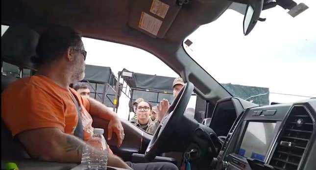 A man sits in a truck while border patrol officers try and speak some sense into him. 