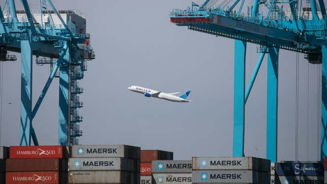 Un avion de United Airlines au décollage vu à travers une pile de conteneurs maritimes et de grues portuaires à Newark, dans le New Jersey