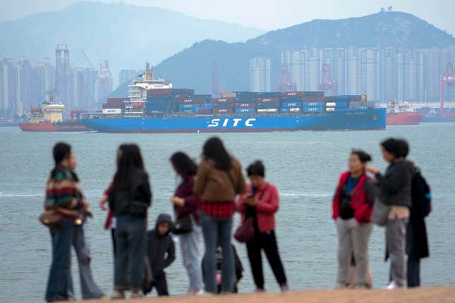 File - A container ship passes tourists in Xiamen in southeast China&#39;s Fujian province on Dec. 26, 2023. Hobbled by high interest rates, persistent inflation, slumping trade and a diminished China, the global economy will slow for a third consecutive year in 2024. (AP Photo/Andy Wong, File)