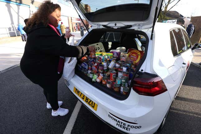 A woman with a bunch of canned goods in the trunk of a white hatchback