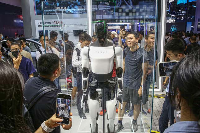 des personnes tenant des téléphones entourent une vitrine avec un robot humanoïde noir et blanc