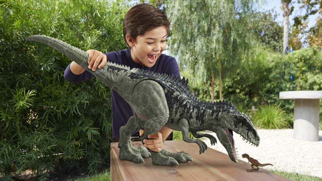 A child plays with a giant dinosaur toy as it hovers its open jaw over a tiny dinosaur toy.