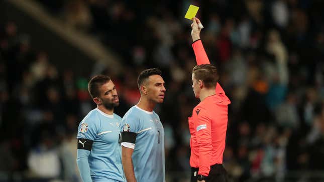 A referee shows a yellow card to two Israeli football players during a UEFA EURO 2024 European qualifier match between Israel and Romania.