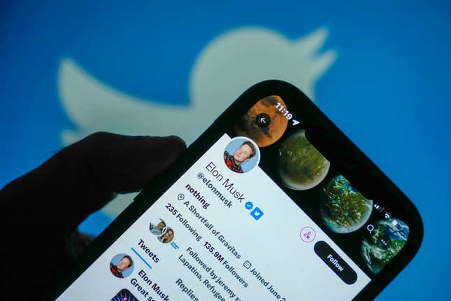 A view of Elon Musk's Twitter account is seen on a mobile cell phone held up against a Twitter logo in the background.