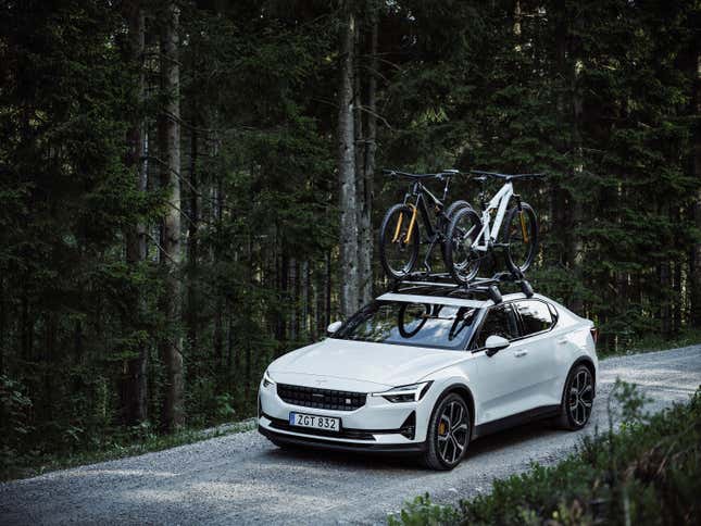 Likely insufferable person driving a white Polestar 2 with bikes on top of it down a gravel road.