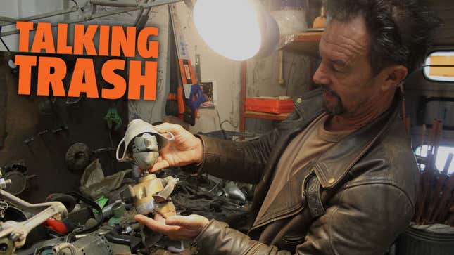 A photo of British artist Joe Rush in his workshop, he is holding parts of an old drill. 