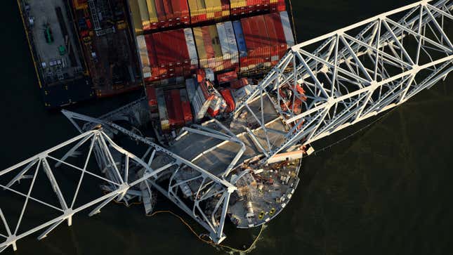 A photo of the front of a container ship stuck under a bridge. 