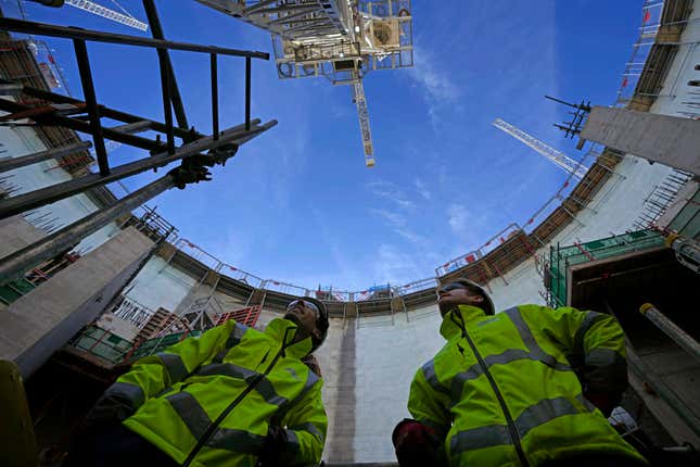 FILE - Employees look up at the construction site of Hinkley Point C nuclear power station in Somerset, England, Tuesday, Oct. 11, 2022. A major nuclear plant that Britain’s government hopes will generate affordable, low-carbon energy could cost up to 46 billion pounds, or $59 billion, and the completion date could be delayed to after 2029. The U.K. government says nuclear projects like the Hinkley Point C plant is a key part of its plans to ensure greater energy independence and achieve its “net zero” by 2050 strategy. (AP Photo/Kin Cheung, File)