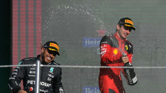 Ferrari driver Charles Leclerc sprays Lewis Hamilton with champagne on a podium.