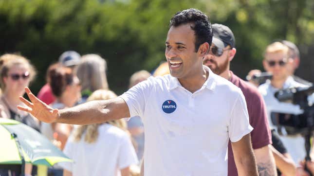 Vivek Ramaswamy waves at a crowd on his presidential campaign. He's wearing a white polo shirt and smiling.