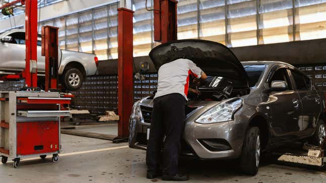 a technician working under the hood of a silver nissan versa in a garage