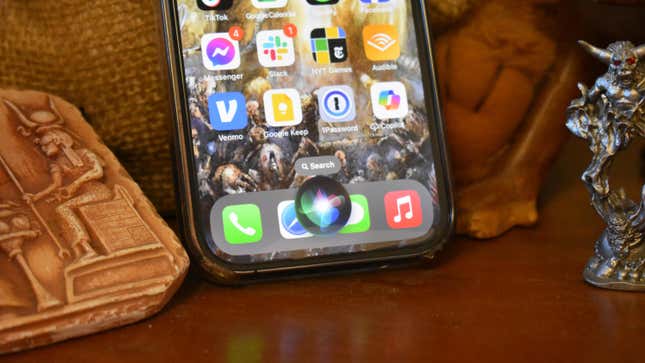 An iPhone 14 Pro showing the Siri icon next to several desk toys.