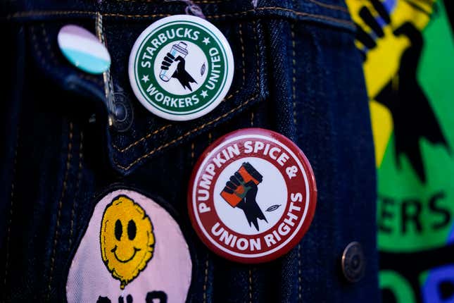 FILE - Employee Quint Palermo wears union pins on their jacket as Starbucks workers participate in a walkout and strike during the company&#39;s Red Cup Day Thursday, Nov. 16, 2023, at the company&#39;s first Reserve roastery in Seattle. The federal government is delaying a new rule that could make it easier for millions of workers to unionize after business groups sued. The National Labor Relations Board says the rule, which was scheduled to go into effect next month, will now be effective Feb. 26 to give it time to resolve legal challenges. (AP Photo/Lindsey Wasson, File)