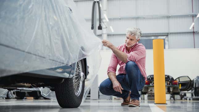 A photo of someone looking under a tarp at their classic car. 