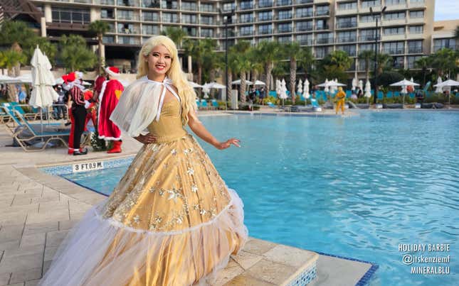 A Holiday Barbie cosplayer smiles with their hand on their hip in front of a hotel pool.