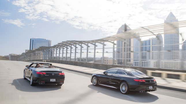 A photo of two Mercedes S Class cars driving past a city skyline. 