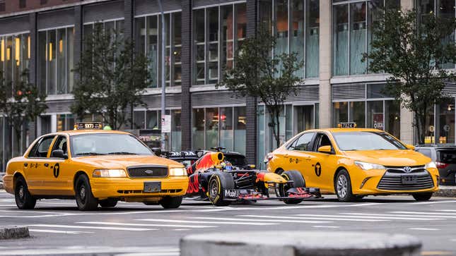 A photo of a Red Bull Formula 1 car lining up alongside two yellow New York City taxis. 