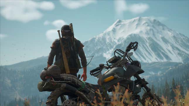 A man stands in front of a mountain and his motorcycle.