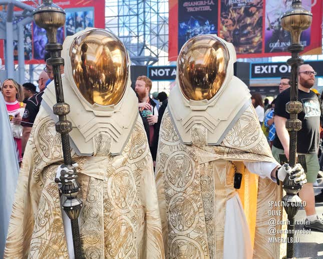 Two cosplayers wear gold face masks and robes.