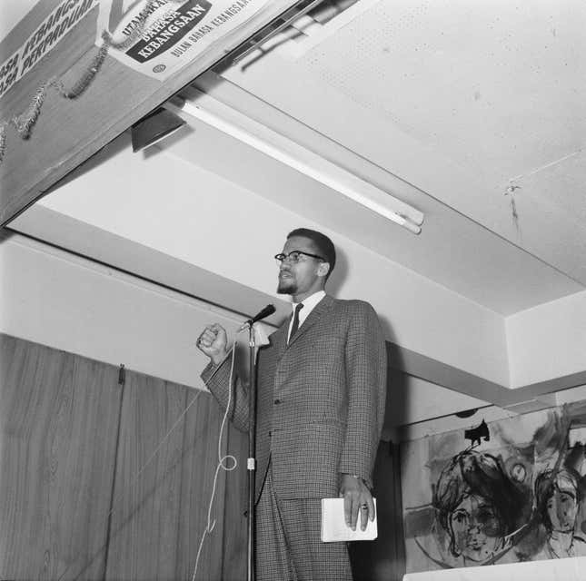 Malcolm X (1925 - 1965) makes a speech, UK, 22nd November 1964. The signs above the stage are in Malay.