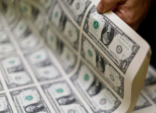 A stack of newly printed uncut US dollars is held up by a hand.