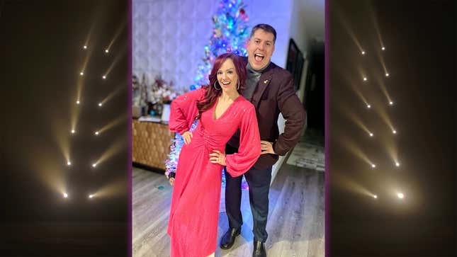 Andrea Rene and John Drake stand smiling in front of a Christmas tree. 