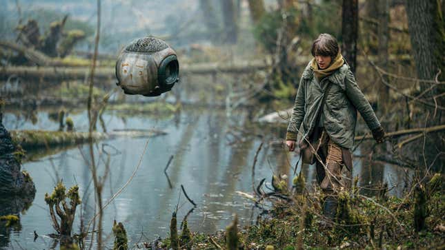 A girl walks through a swamp with a floating robot.