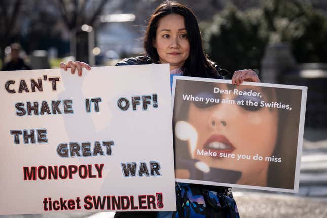 A person demonstrates against Ticketmaster holding two signs. One reads "Can't shake it off! The great monopoly war ticket swindler!" The other reads "Dear Reads, When you aim at the Swifties, make sure you do miss."
