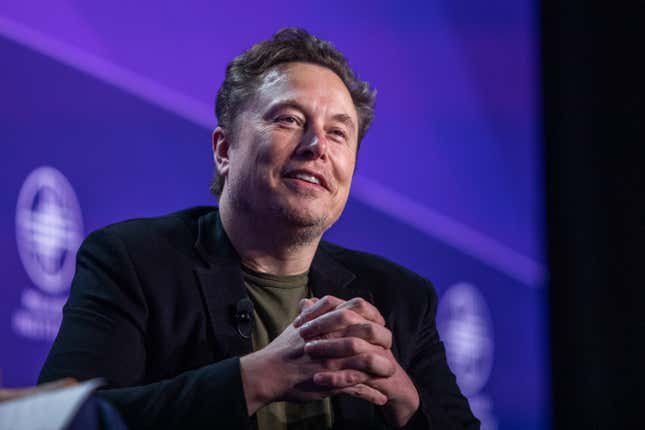 Elon Musk clasping his hands together smiling