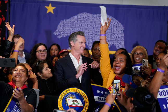 California Gov. Gavin Newsom signs the fast food bill surrounded by fast food workers at the SEIU Local 721 in Los Angeles, on Thursday, Sept. 28, 2023. California fast food workers will be paid at least $20 per hour next year under the new law signed by Newsom. Anneisha Williams, right, who works at a Jack in the Box restaurant in Southern California celebrates as she holds up the bill. (AP Photo/Damian Dovarganes)