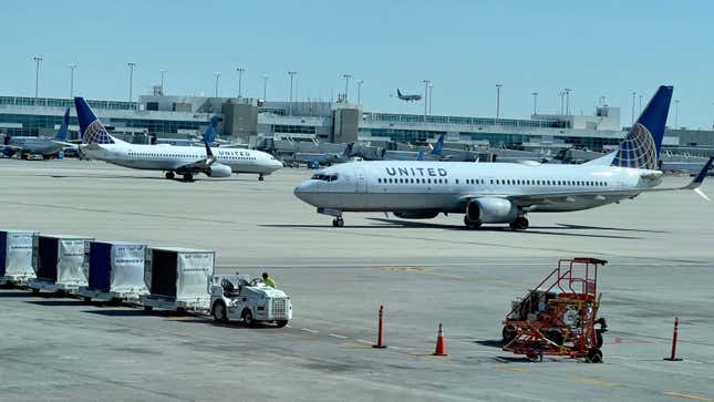 United Airlines planes sit on a tarmac, with baggage handlers working in the foreground. 