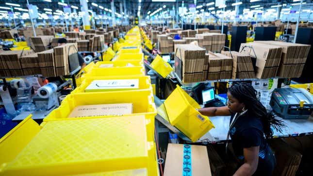 A Amazon warehouse worker stands by a conveyor belt as they put packages onto the line.