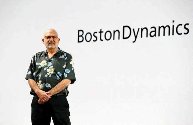 Marc Raibert standing with his hands together in front of a white display that says Boston Dynamics