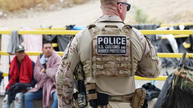 A Customs and Border Protection officer keeps watch as immigrants are transported from a makeshift camp between border walls between the U.S. and Mexico on May 13, 2023 in San Diego, California.