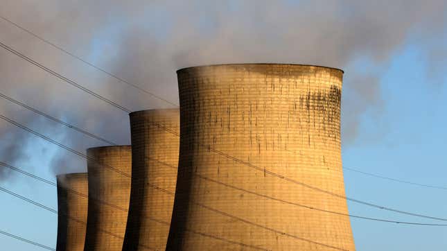 nuclear reactors with smoke coming out the top against a blue sky and crossed by power lines