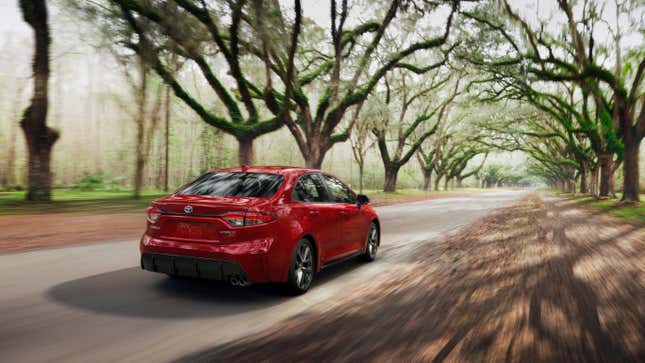 A red corolla hybrid driving down a tree-lined road