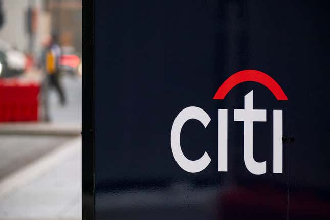 Close-up of a Citi logo on a black background with an out-of-focus street in the back