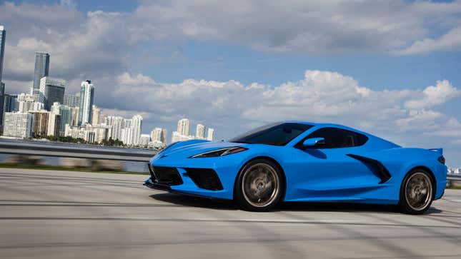 A blue Corvette driving in front of a cityscape