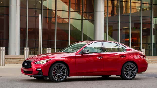 A bright red Infiniti Q50 parked in front of a glass building