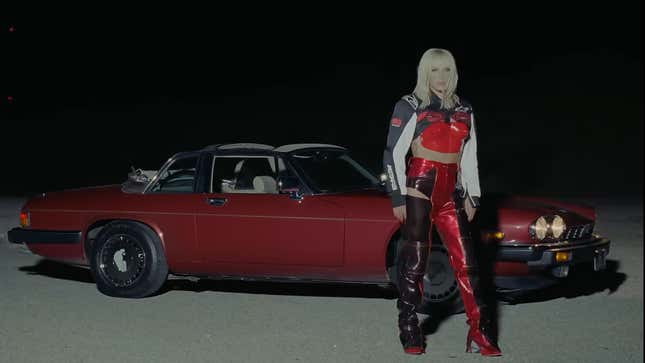 a screenshot of Kesha standing in front of the red Jaguar XJ-SC at night