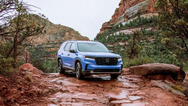 A blue Honda Pilot off-roading on some rocks in a place that looks like Utah with reddish rocks and pine trees