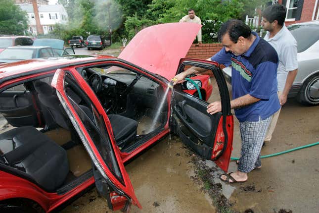 A man hosing out the interior of his red car after a flood