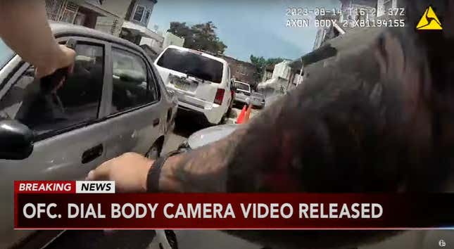 A tattooed arm is reaching for a car door while another hand is pointing the a gun directly into a car.