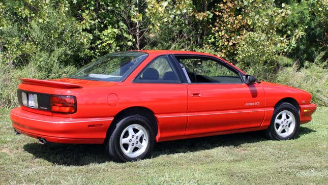 Une Oldsmobile Achieva SCX W41 rouge garée sur l’herbe depuis l’arrière, à 3/4