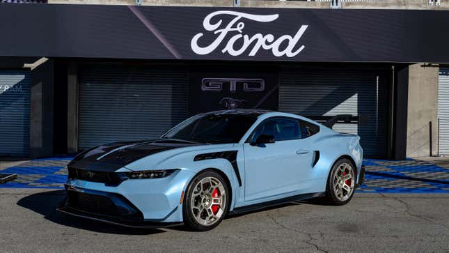 A light blue Ford Mustang GTD parked in front of a racing garage