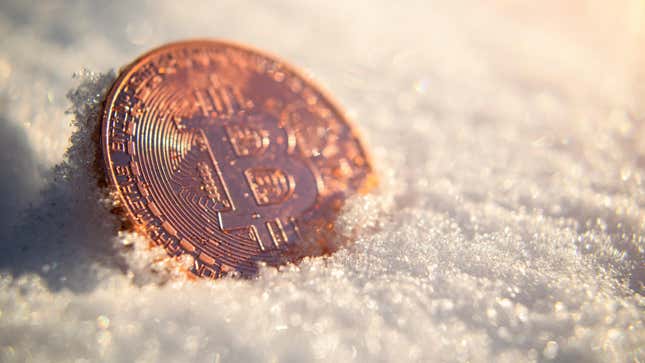 A coin with the bitcoin logo submerged in some snow.