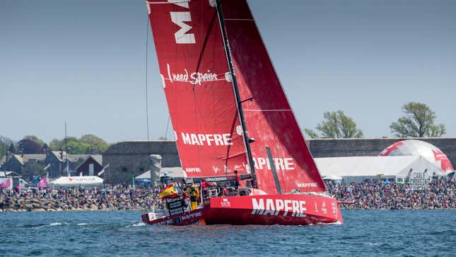 a giant red MAPFRE sailboat sailing toward a crowd