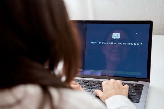 back view of woman with dark hair typing on a laptop, a virtual assistant is displayed on the screen