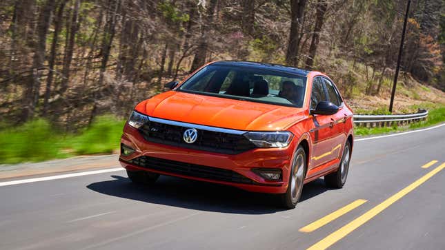 A photo of an orange VW Jetta driving down a highway. 