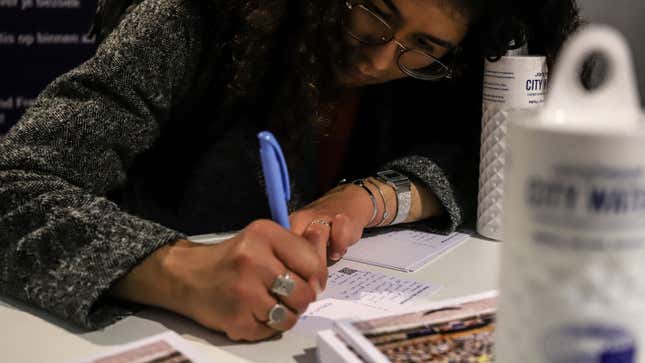 A photo of a person writing a note while sat at a table. 